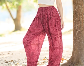 May include: A woman wearing a white crop top and loose, patterned, burgundy pants. The pants feature a circular design. The person is standing near a tree in a park-like setting, with sunlight filtering through the leaves.