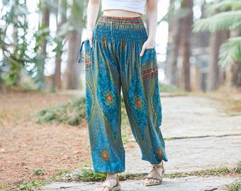May include: A woman wearing a white crop top and blue patterned pants with an elastic waistband. She is standing on a paved path in a forest setting.