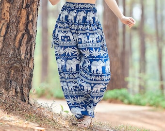 Puede incluir: Una mujer con un top blanco corto y pantalones azules con estampado de elefante se encuentra en un bosque. Está sonriendo y mirando hacia el cielo.