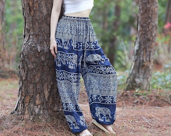 Puede incluir: Una mujer con un top blanco corto y pantalones azules estampados se encuentra en un bosque. Se apoya en el tronco de un árbol.