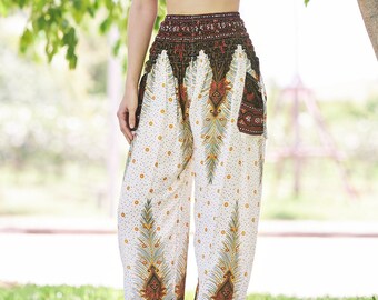 May include: A woman wearing a black sports bra and white pants with a brown and green floral pattern. The pants have a wide leg and are gathered at the waist. She is standing in a grassy area with trees in the background.
