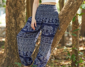 Puede incluir: Una mujer con un top blanco sin mangas y pantalones azules con estampado de elefantes. Está de pie en un bosque con árboles detrás de ella.