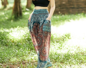 May include: A woman wearing a black crop top and patterned teal and rust-colored harem pants with pockets. The pants feature a mandala-style design. The background is a lush green forest with sunlight filtering through the trees.