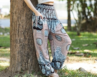 May include: A woman wearing a white tank top and patterned pants stands with her eyes closed and head tilted back, enjoying the fresh air in a park setting.