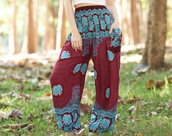 Op de afbeelding: Een vrouw draagt een wit tanktop en een rode broek met een blauwe en witte olifantenprint. De broek is losjes gesneden en heeft wijde pijpen.
