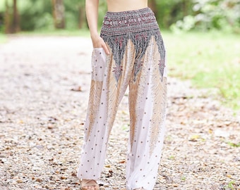 May include: A woman wearing a black sports bra and white printed pants with a high waist. The pants have a wide leg and a flowing design. The woman is standing on a path in a forest.