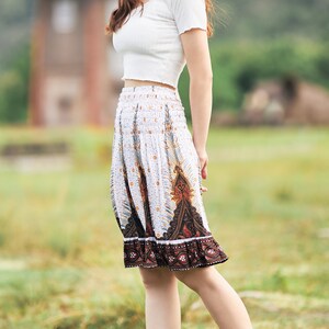 K&ouml;nnte beinhalten: Eine Frau tr&auml;gt ein wei&szlig;es Crop-Top und einen wei&szlig;en Rock mit braunem Muster. Sie steht auf einem Feld mit gr&uuml;nem Gras.