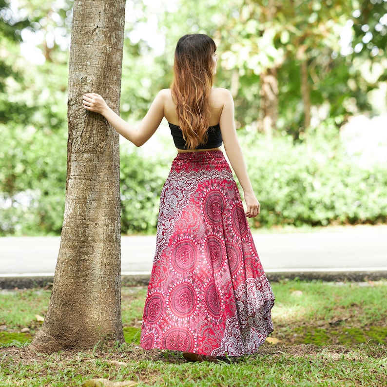 Pode incluir: Uma mulher vestindo uma saia maxi estampada em vermelho e branco com um top preto. Ela est&aacute; em p&eacute; ao lado de uma &aacute;rvore em um parque.