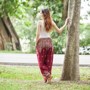 K&ouml;nnte beinhalten: Ein wei&szlig;es Tanktop kombiniert mit einer locker sitzenden, dunkelroten Pluderhose mit einem komplexen goldfarbenen Muster. Die Hose hat einen breiten, elastischen Bund und ein zulaufendes Bein mit einem floralen Motiv und dekorativen Bord&uuml;ren.