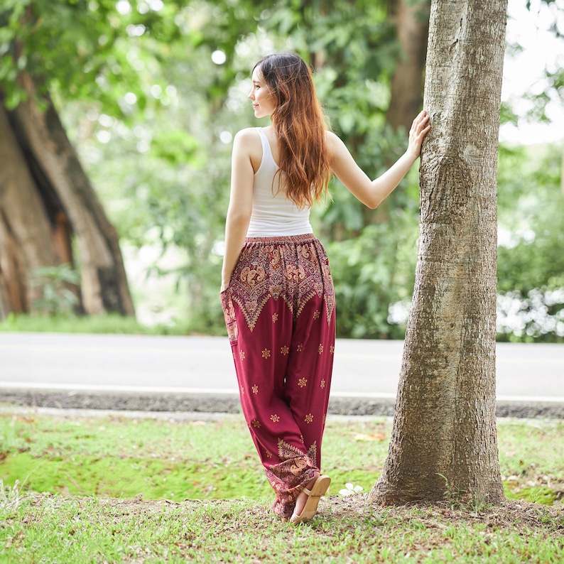 K&ouml;nnte beinhalten: Ein wei&szlig;es Tanktop kombiniert mit einer locker sitzenden, dunkelroten Pluderhose mit einem komplexen goldfarbenen Muster. Die Hose hat einen breiten, elastischen Bund und ein zulaufendes Bein mit einem floralen Motiv und dekorativen Bord&uuml;ren.