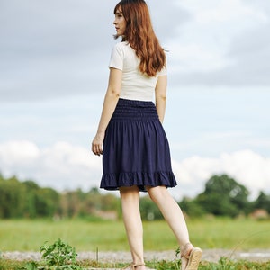 Op de afbeelding: Een vrouw in een wit T-shirt en een donkerblauwe rok loopt over een houten pad in een veld.