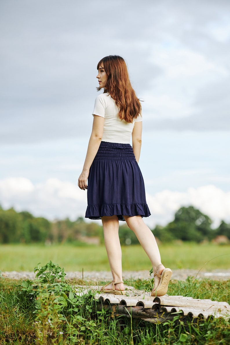 Op de afbeelding: Een vrouw in een wit T-shirt en een donkerblauwe rok loopt over een houten pad in een veld.