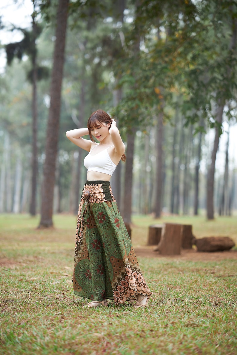 Puede incluir: Una mujer con un top corto blanco y una falda larga estampada. La falda presenta un dise&ntilde;o floral verde y marr&oacute;n y est&aacute; atada a la cintura. El fondo muestra un bosque con &aacute;rboles altos y hierba.