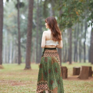 Puede incluir: Falda larga y fluida con un estampado floral verde y marr&oacute;n. La falda se combina con un top corto blanco. La imagen est&aacute; tomada al aire libre en un entorno forestal, con &aacute;rboles al fondo.