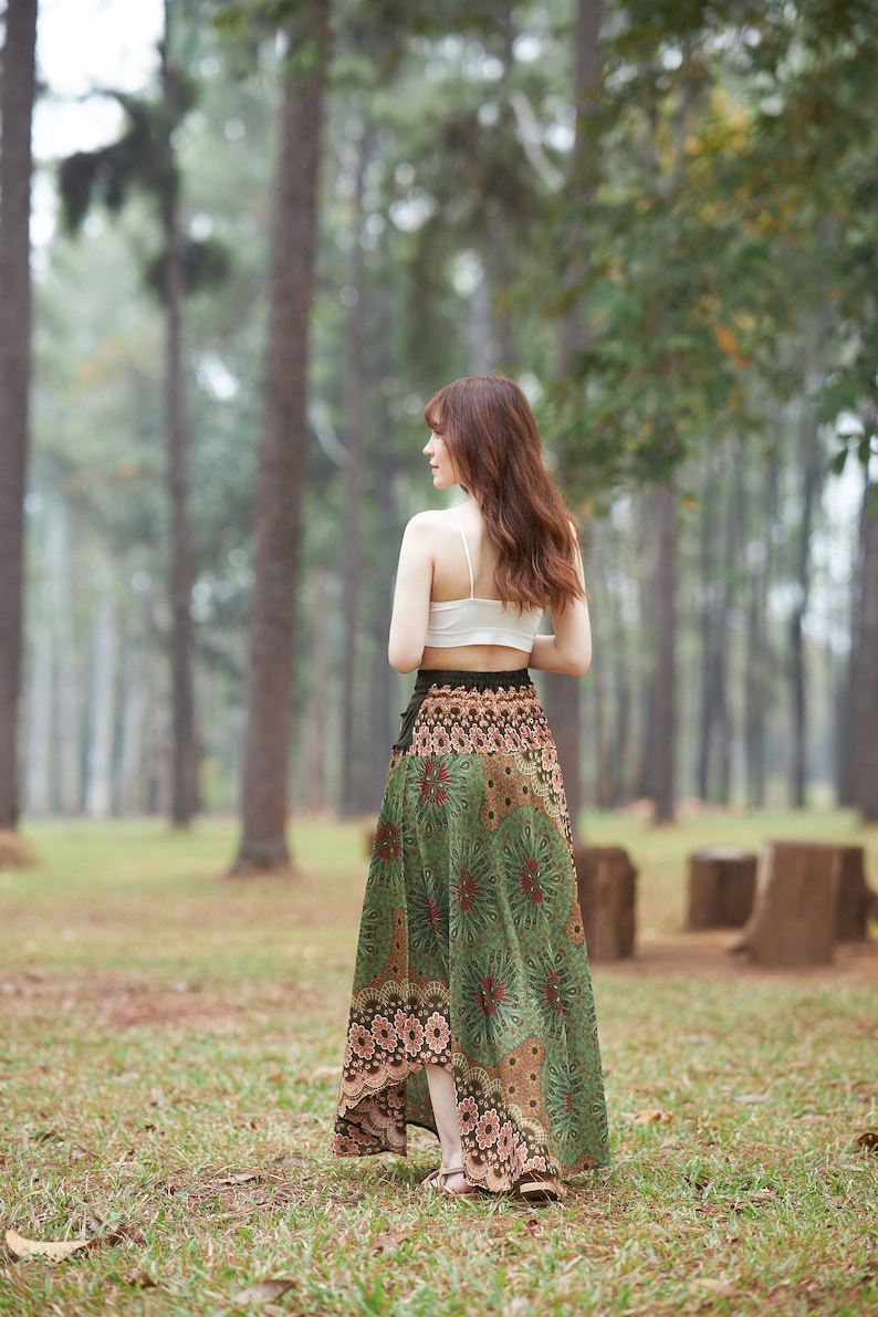 Puede incluir: Falda larga y fluida con un estampado floral verde y marr&oacute;n. La falda se combina con un top corto blanco. La imagen est&aacute; tomada al aire libre en un entorno forestal, con &aacute;rboles al fondo.