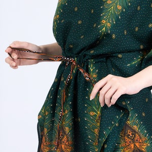 K&ouml;nnte beinhalten: Eine gr&uuml;ne Kaftan mit einem Pfauenfeder-Druck und orange-schwarzem Paisley-Besatz. Die Kaftan hat eine Kordeltaille und einen V-Ausschnitt.