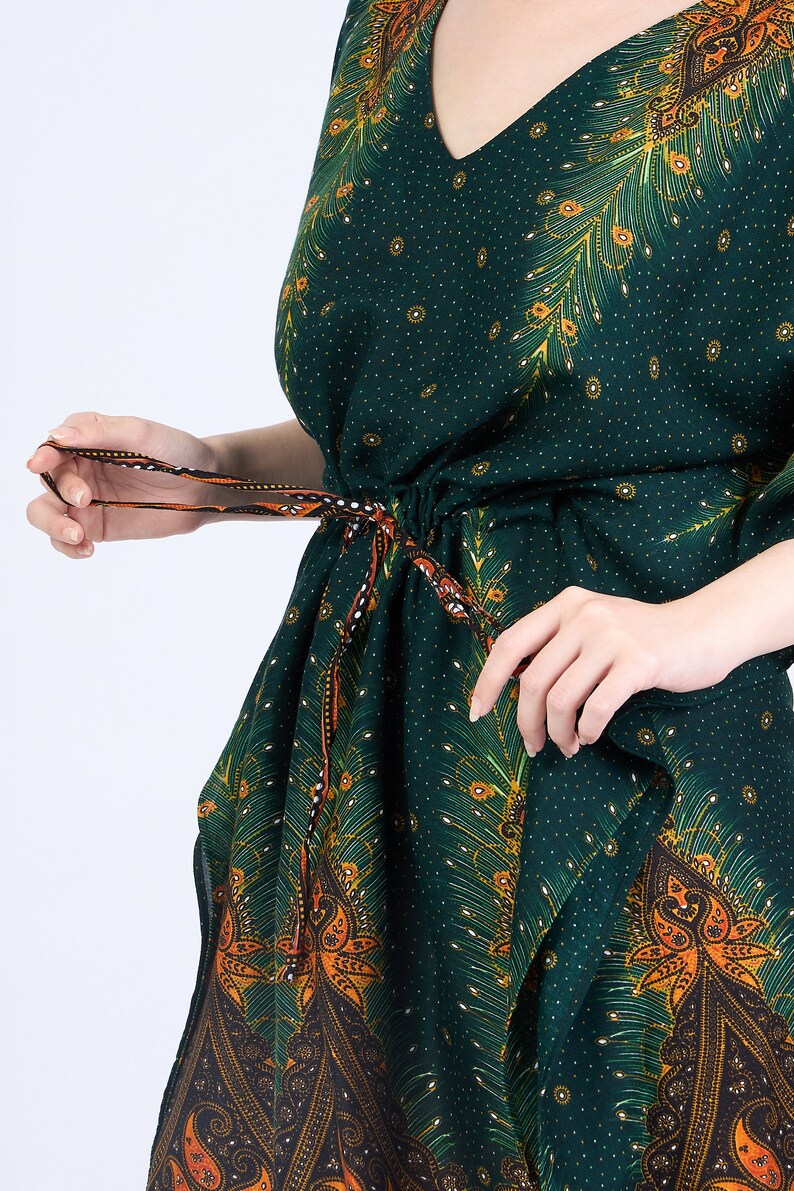 K&ouml;nnte beinhalten: Eine gr&uuml;ne Kaftan mit einem Pfauenfeder-Druck und orange-schwarzem Paisley-Besatz. Die Kaftan hat eine Kordeltaille und einen V-Ausschnitt.