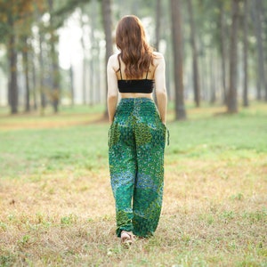 Puede incluir: Una mujer con un top negro corto y pantalones verdes estampados camina por un bosque.