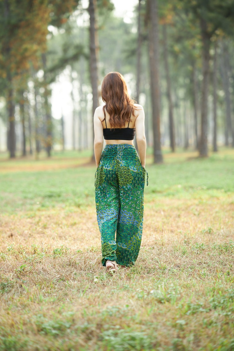 Puede incluir: Una mujer con un top negro corto y pantalones verdes estampados camina por un bosque.