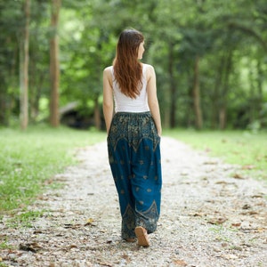 K&ouml;nnte beinhalten: Ein wei&szlig;es &auml;rmelloses Tanktop kombiniert mit einer locker sitzenden, blaugr&uuml;nen Hose mit einem komplizierten goldenen und dunkelblauen Paisley-Muster, einem breiten elastischen Bund und Seitentaschen, von hinten gesehen.