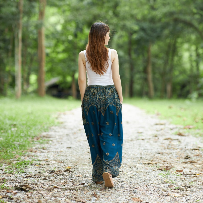 K&ouml;nnte beinhalten: Ein wei&szlig;es &auml;rmelloses Tanktop kombiniert mit einer locker sitzenden, blaugr&uuml;nen Hose mit einem komplizierten goldenen und dunkelblauen Paisley-Muster, einem breiten elastischen Bund und Seitentaschen, von hinten gesehen.