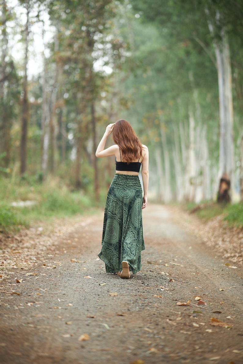Op de afbeelding: Een zwarte crop top met spaghettibandjes gecombineerd met een lange, zwierige groene rok met een donker, ingewikkeld cirkelvormig mandalapatroon en een brede, gesmokte elastische tailleband die hoog in de taille zit voor een losse pasvorm.