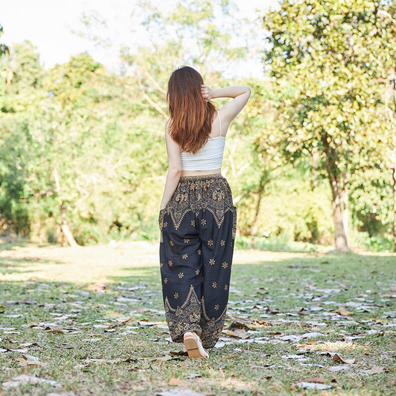 K&ouml;nnte beinhalten: Ein wei&szlig;es &auml;rmelloses bauchfreies Oberteil kombiniert mit einer weiten schwarzen Pluderhose mit einem detaillierten gold- und beigefarbenen Paisleymuster. Die Hose hat einen hohen elastischen Bund und ein weit geschnittenes Bein.