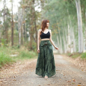 Op de afbeelding: Een zwarte crop top met spaghettibandjes gecombineerd met een high-waisted broek met wijde pijpen in een donkergroene stof met een gedetailleerde zwarte mandala-print en een opvallende ronde houten gesp in de tailleband.