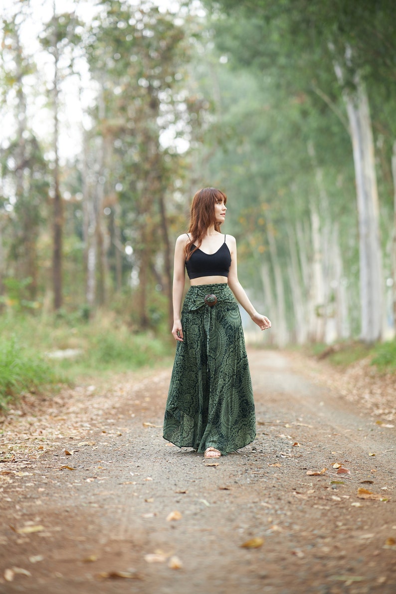 Op de afbeelding: Een zwarte crop top met spaghettibandjes gecombineerd met een high-waisted broek met wijde pijpen in een donkergroene stof met een gedetailleerde zwarte mandala-print en een opvallende ronde houten gesp in de tailleband.