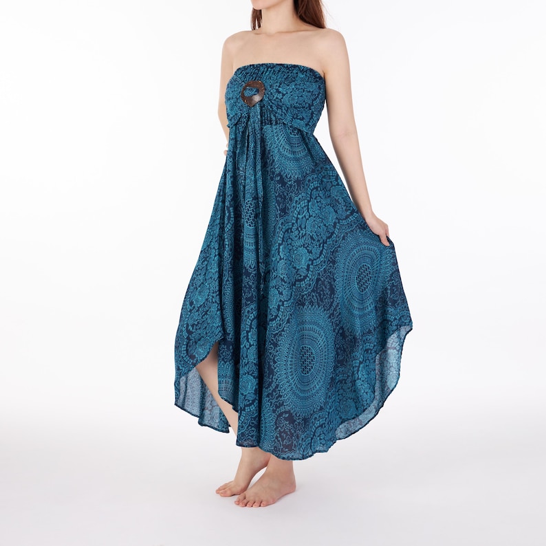 Op de afbeelding: Een strapless midi-jurk in blauwgroen en donkerblauw met een herhalend cirkelvormig mandalapatroon. Het lijfje is geplooid met een elastische bovenkant en heeft een donkerbruine ronde houten ring als accent in het midden.