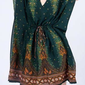 K&ouml;nnte beinhalten: Eine gr&uuml;ne, kurz&auml;rmelige Kaftan mit einem Pfauenfeder-Druck und orangefarbenen und braunen Akzenten. Die Kaftan hat eine Kordelzugtaille und einen V-Ausschnitt.