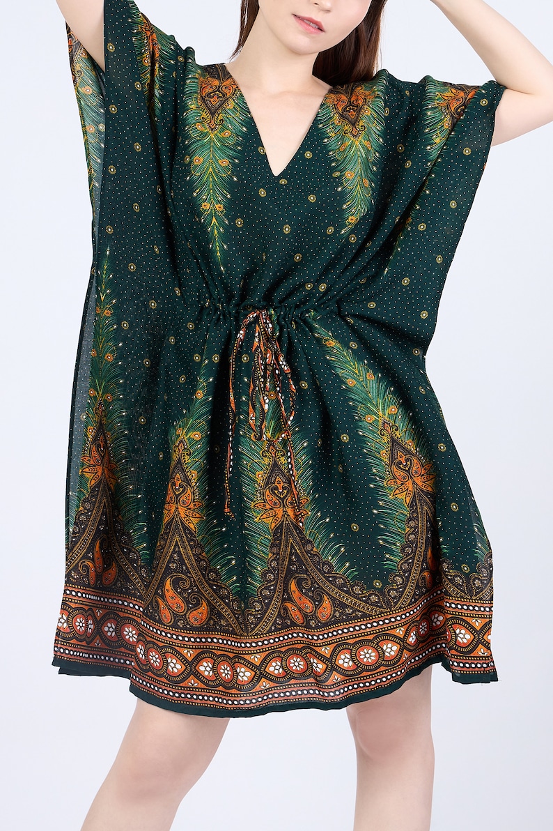 K&ouml;nnte beinhalten: Eine gr&uuml;ne, kurz&auml;rmelige Kaftan mit einem Pfauenfeder-Druck und orangefarbenen und braunen Akzenten. Die Kaftan hat eine Kordelzugtaille und einen V-Ausschnitt.
