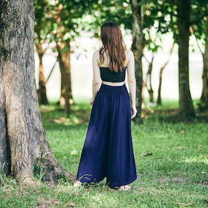 K&ouml;nnte beinhalten: Eine Frau in einem schwarzen Crop-Top und einer dunkelblauen weiten Hose steht in einer Waldlandschaft.