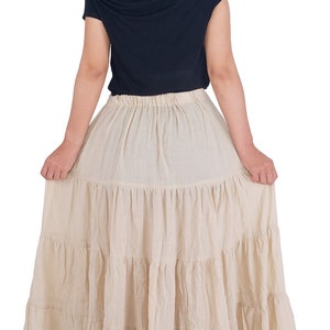 May include: A beige tiered maxi skirt with a gathered elastic waistband. The skirt is made of a lightweight, flowy fabric.