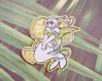 Puede incluir: Una pegatina holográfica con una sirena de pelo largo, que lleva una corona y un vestido. La sirena está sentada sobre su cola con las manos juntas. La pegatina tiene un fondo dorado con una forma de corazón en la esquina superior izquierda.