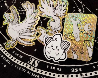 Puede incluir: Cuatro pegatinas holográficas con diferentes personajes de Pokemon. Las pegatinas están sobre un fondo negro con estrellas blancas. Las pegatinas son de diferentes tamaños y formas. Las pegatinas son todas doradas y blancas.