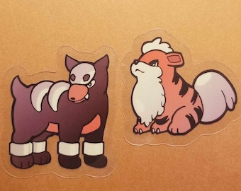 Puede incluir: Dos pegatinas de dibujos animados de personajes de Pokemon. La primera pegatina es de un Pokemon parecido a un perro, de color morado y rojo, con una franja blanca en la espalda. La segunda pegatina es de un Pokemon parecido a un perro, de color rosa y naranja, con una melena y cola blancas.