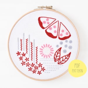 May include: Embroidered hoop art with a red and pink floral design. The design includes a large flower, leaves, and smaller flowers. The hoop is made of wood and has a white background. The text "PDF PATTERN" is in a yellow circle in the lower right corner.