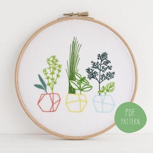 May include: Embroidered herb garden design in a wooden hoop. The artwork features three different herbs in geometric pots, with green leaves and colorful thread. The text "PDF PATTERN" is on a green circle.