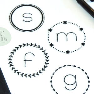 May include: A PDF pattern for embroidery designs featuring four different monogram initials: S, M, F, and G. Each initial is surrounded by a unique decorative border.