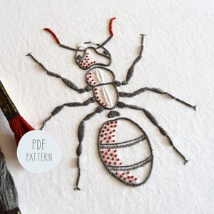 May include: Embroidered ant design with a gray body and red accents. The ant is stitched on white fabric. The text "PDF PATTERN" is written in a circle on the fabric.