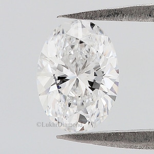 May include: A clear oval-shaped diamond held by tweezers. The diamond is faceted and reflects light.