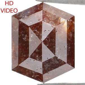 May include: A hexagonal, reddish-brown diamond held by tweezers. The gem has a geometric pattern within its structure. The words "HD VIDEO" are in the upper left corner. The diamond's facets reflect light, showcasing its clarity and cut.