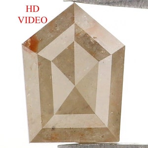 May include: A pentagonal-shaped loose diamond with a light brown, champagne hue and visible internal inclusions. The gemstone features a faceted surface with a pointed top and a flat base, displaying a mix of translucent and opaque areas.