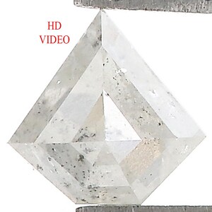 Könnte beinhalten: Ein klarer, rautenförmiger Diamant, der von einer Metallpinzette gehalten wird. Der Diamant hat einen facettierten Schliff mit sichtbaren Einschlüssen und einen leicht grauen Farbton. Der Text "HD VIDEO" ist rot.
