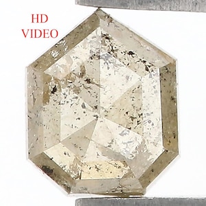 Può includere: Un diamante sale e pepe sciolto con taglio esagonale, caratterizzato da una tavolozza di colori traslucidi, grigio chiaro e beige con inclusioni interne e sfaccettature visibili. Il testo HD VIDEO è stampato in rosso sul lato sinistro.