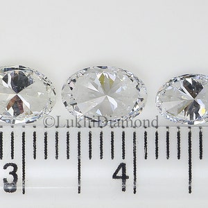 May include: Nine clear oval-shaped gemstones of varying sizes are lined up on a ruler, with the largest gemstone measuring approximately 7/8 inch in diameter.