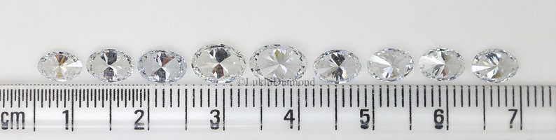 May include: Nine clear oval-shaped gemstones of varying sizes are lined up on a ruler, with the largest gemstone measuring approximately 7/8 inch in diameter.