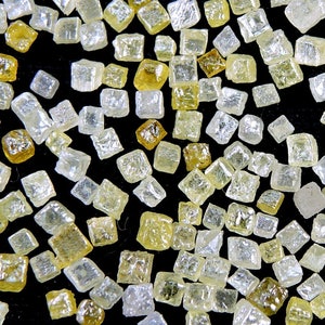 May include: Close-up of a collection of small, clear and yellow cubic crystals. The crystals are scattered on a black surface.