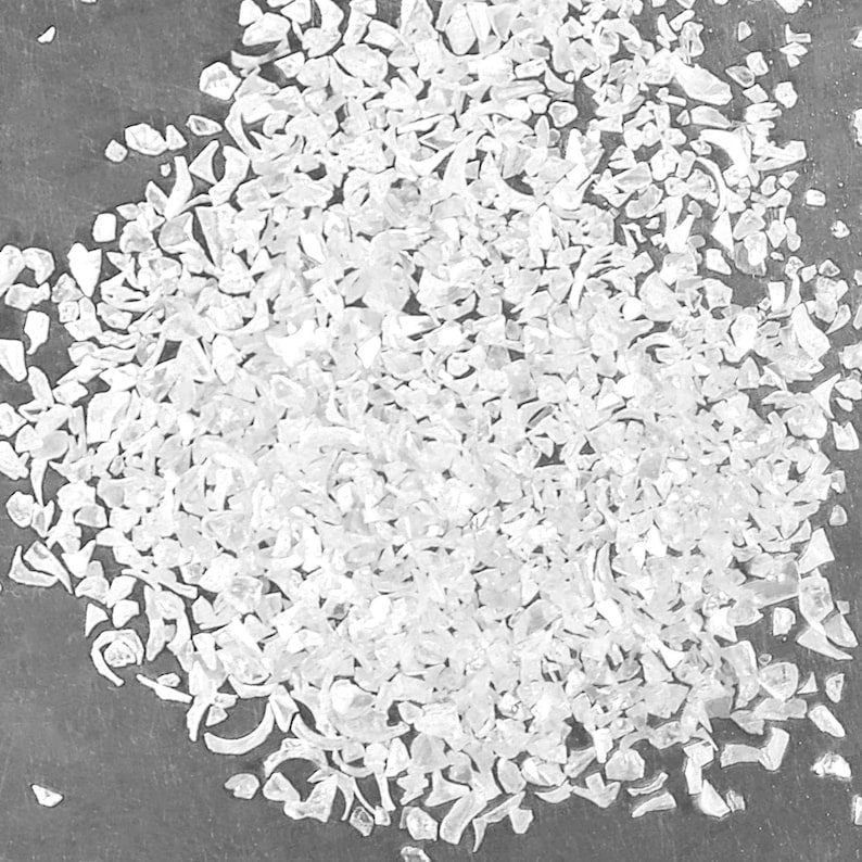 Pu&ograve; includere: Una collezione di piccoli frammenti di vetro frantumato bianco e traslucido con forme irregolari e bordi taglienti. I pezzi variano in dimensioni e sono sparsi in un denso ammasso, riflettendo la luce per creare un aspetto luminoso e strutturato.